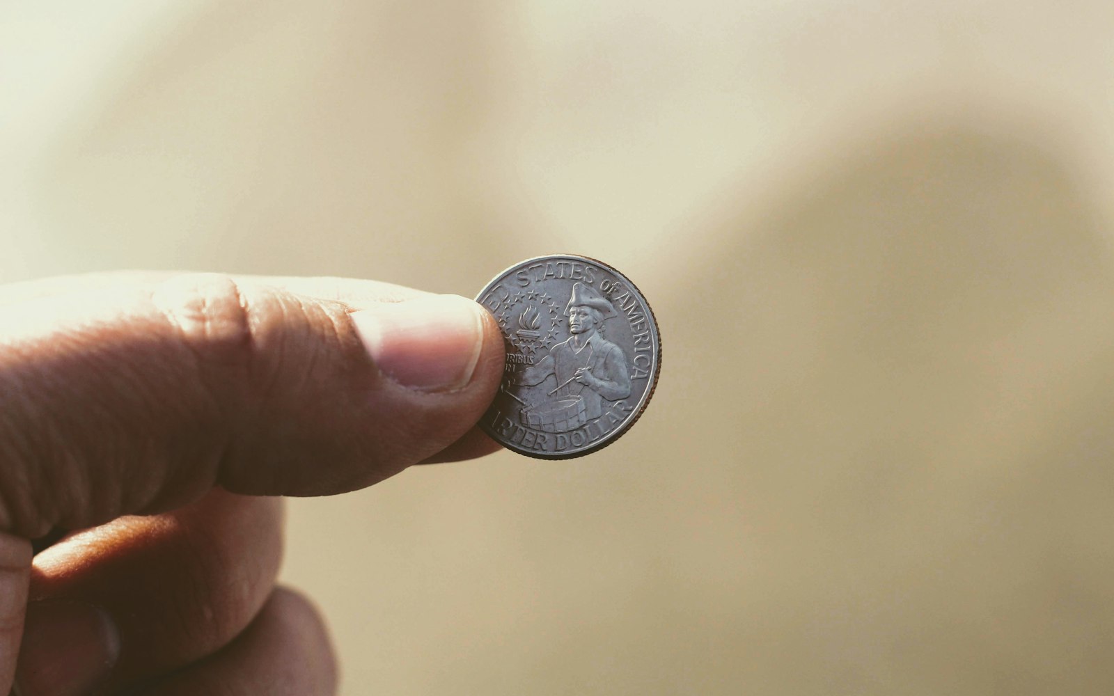 A quarter balanced upright on a fingertip, one face turned to the camera and the other out of sight