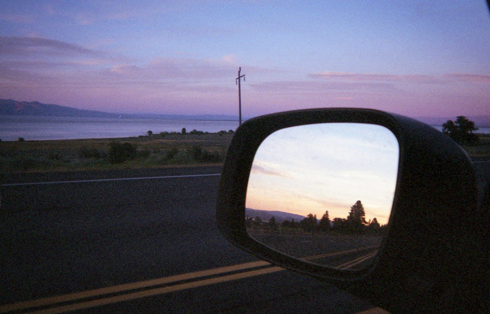 A car's side mirror at dusk, reflecting the road behind. Photo by Kimson Doan on Unsplash