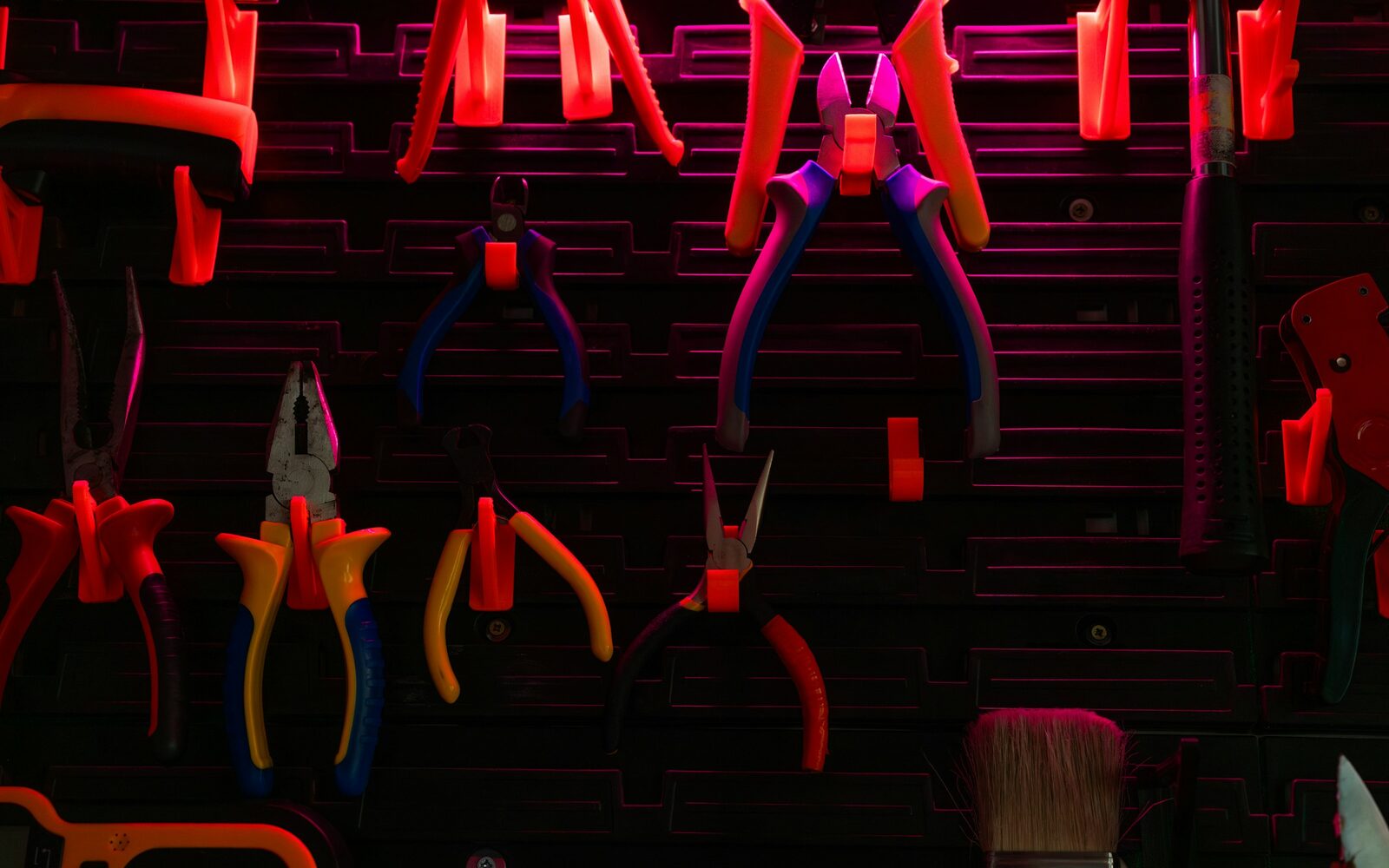 A dark workshop slat wall under neon light, every hand tool clipped into a holder of its own