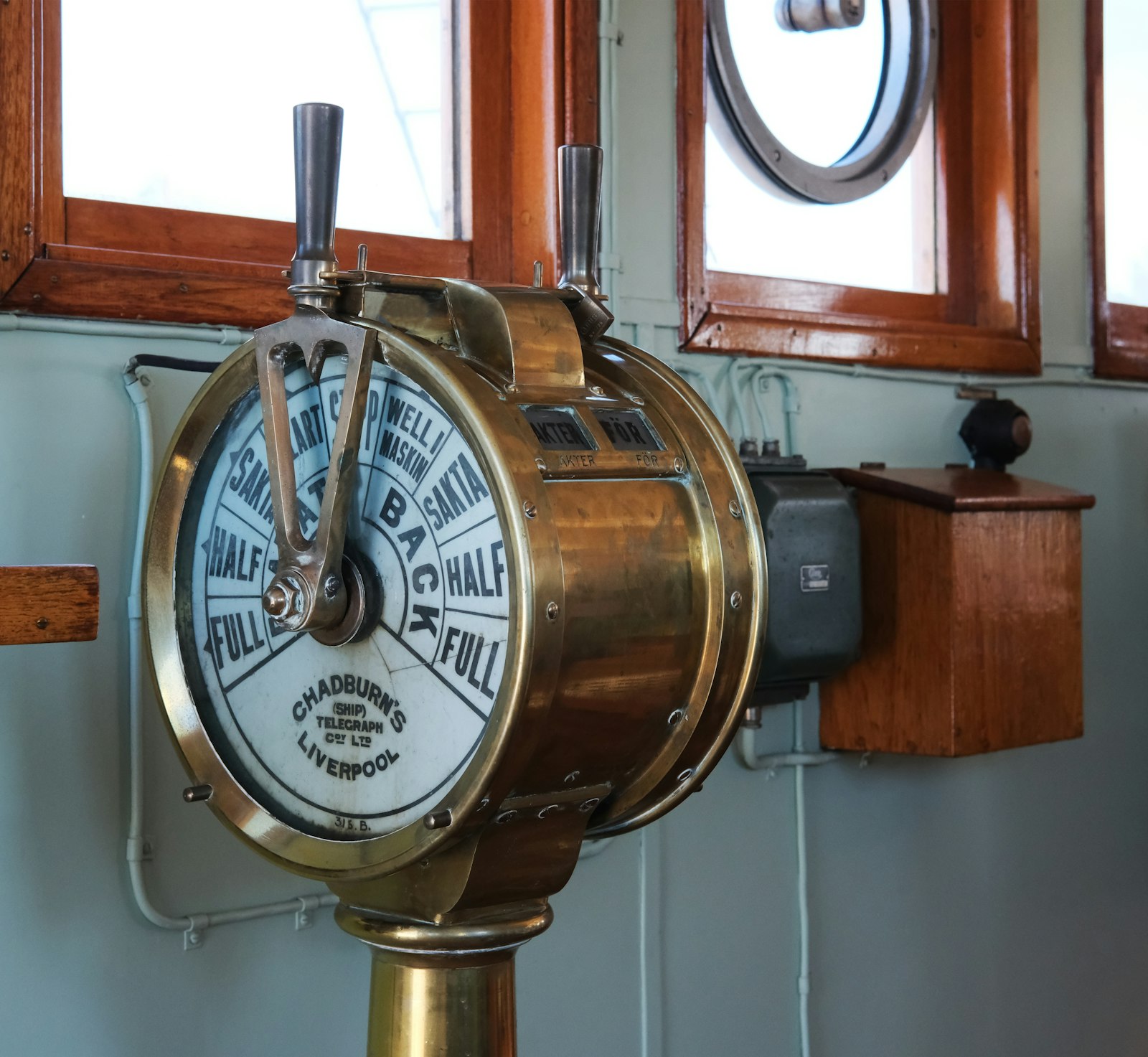 A brass ship's engine-order telegraph on a bridge — a fixed dial of commands selected by a lever